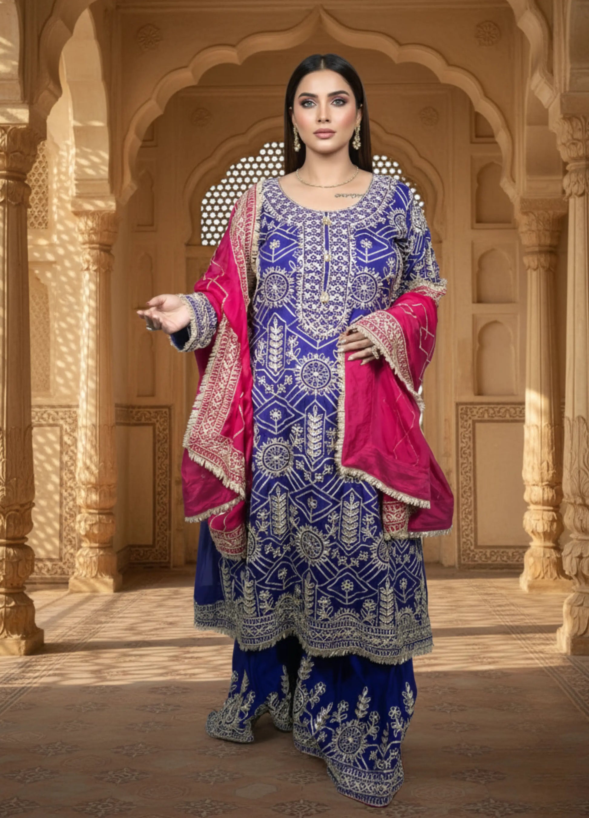 Woman in a traditional blue and pink outfit standing in an ornate architectural setting.