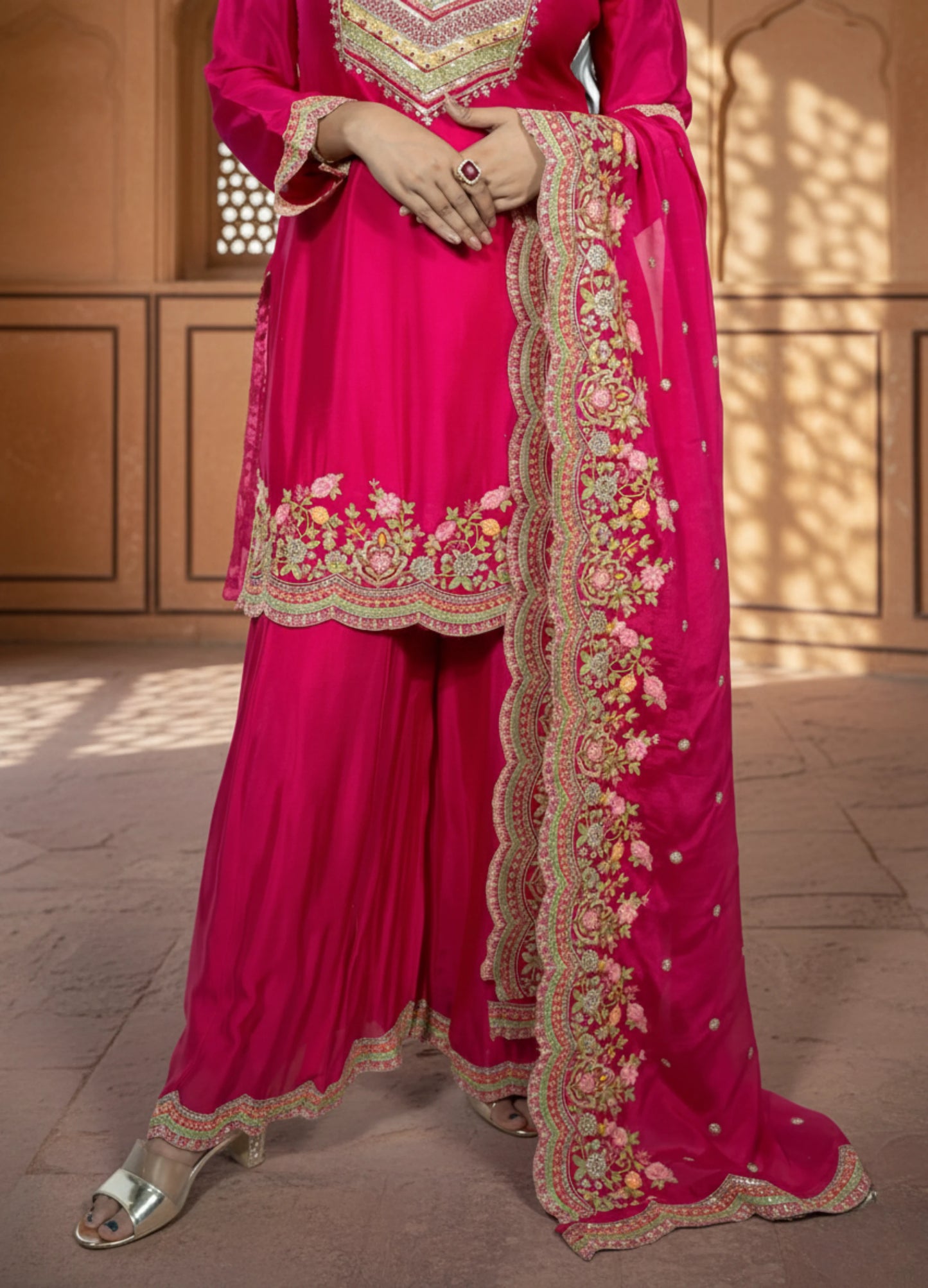 Pink traditional outfit with intricate embroidery on a wooden floor.