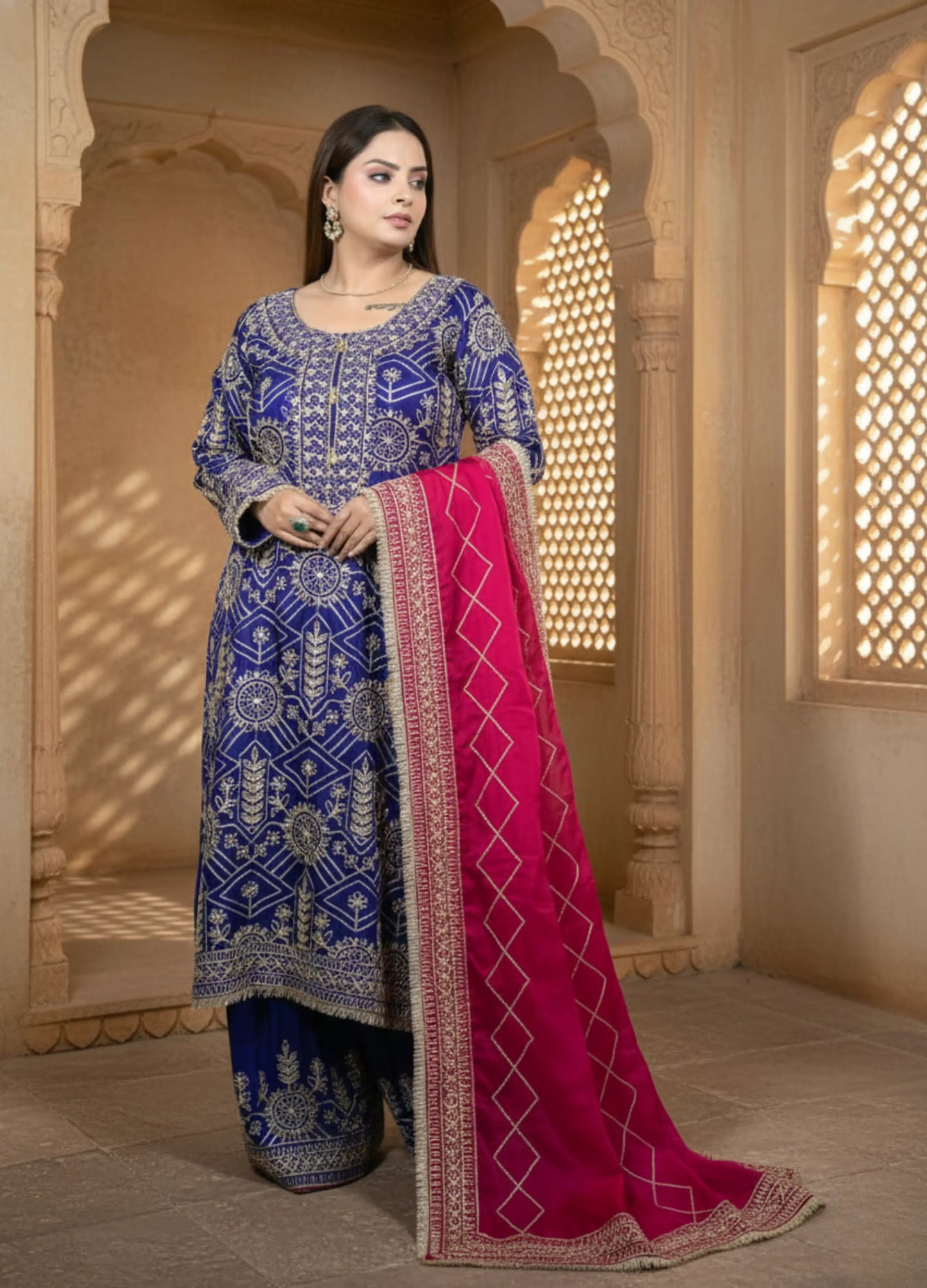 Woman in a blue embroidered traditional outfit with a pink dupatta in an ornate setting