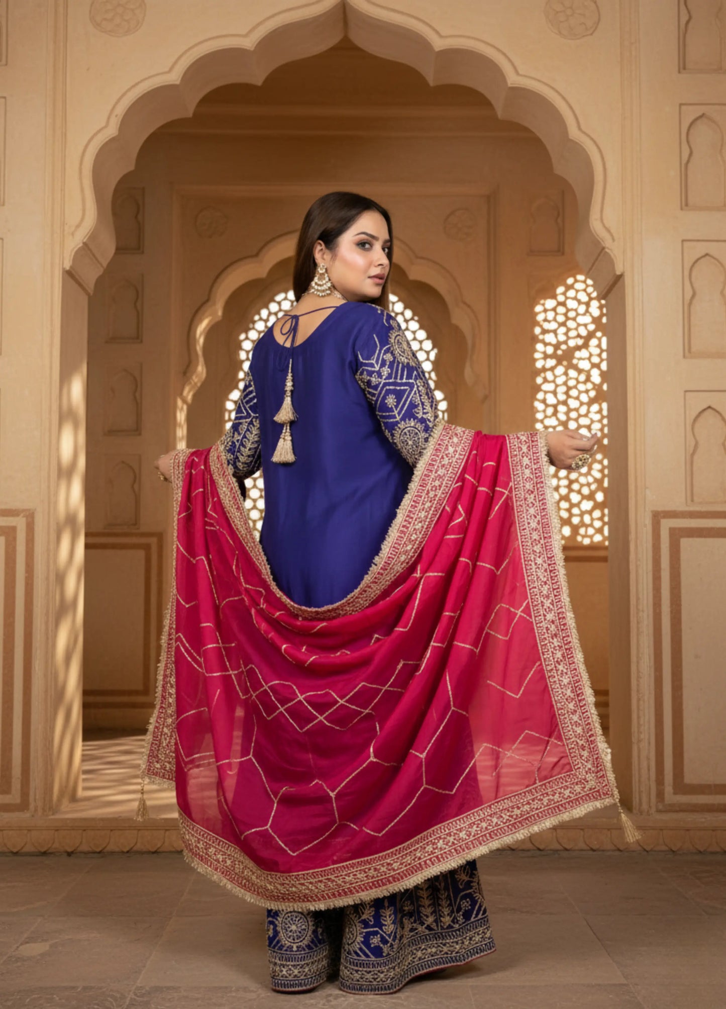 Woman in traditional blue and pink outfit with intricate patterns in a decorative setting