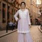 Woman in a light purple and white traditional outfit standing on a cobbled street with historical buildings.