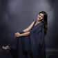 Woman in a dark blue saree sitting against a black background