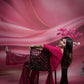 Woman in a pink dress standing next to a decorative chair against a pink background