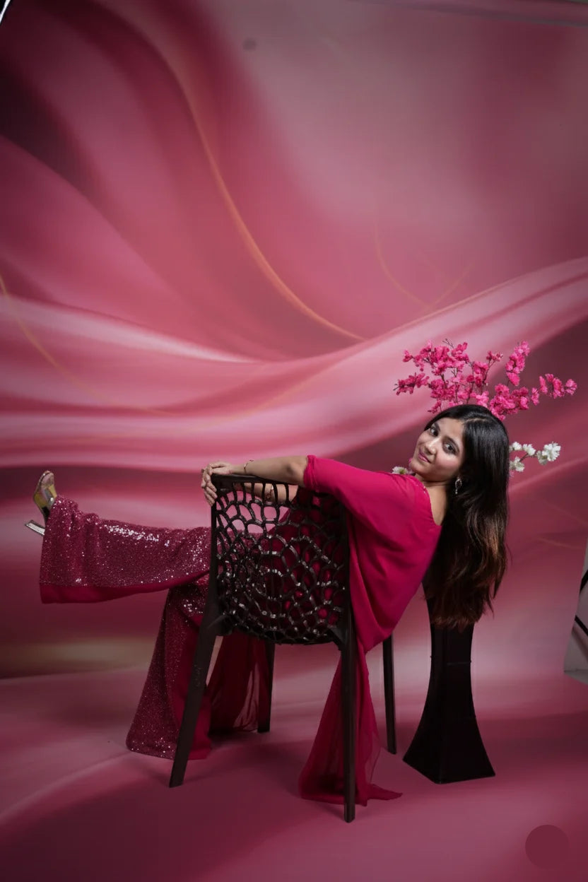 Woman in a pink dress standing next to a decorative chair against a pink background