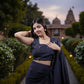 Woman in a dark blue saree standing in a garden with a temple in the background