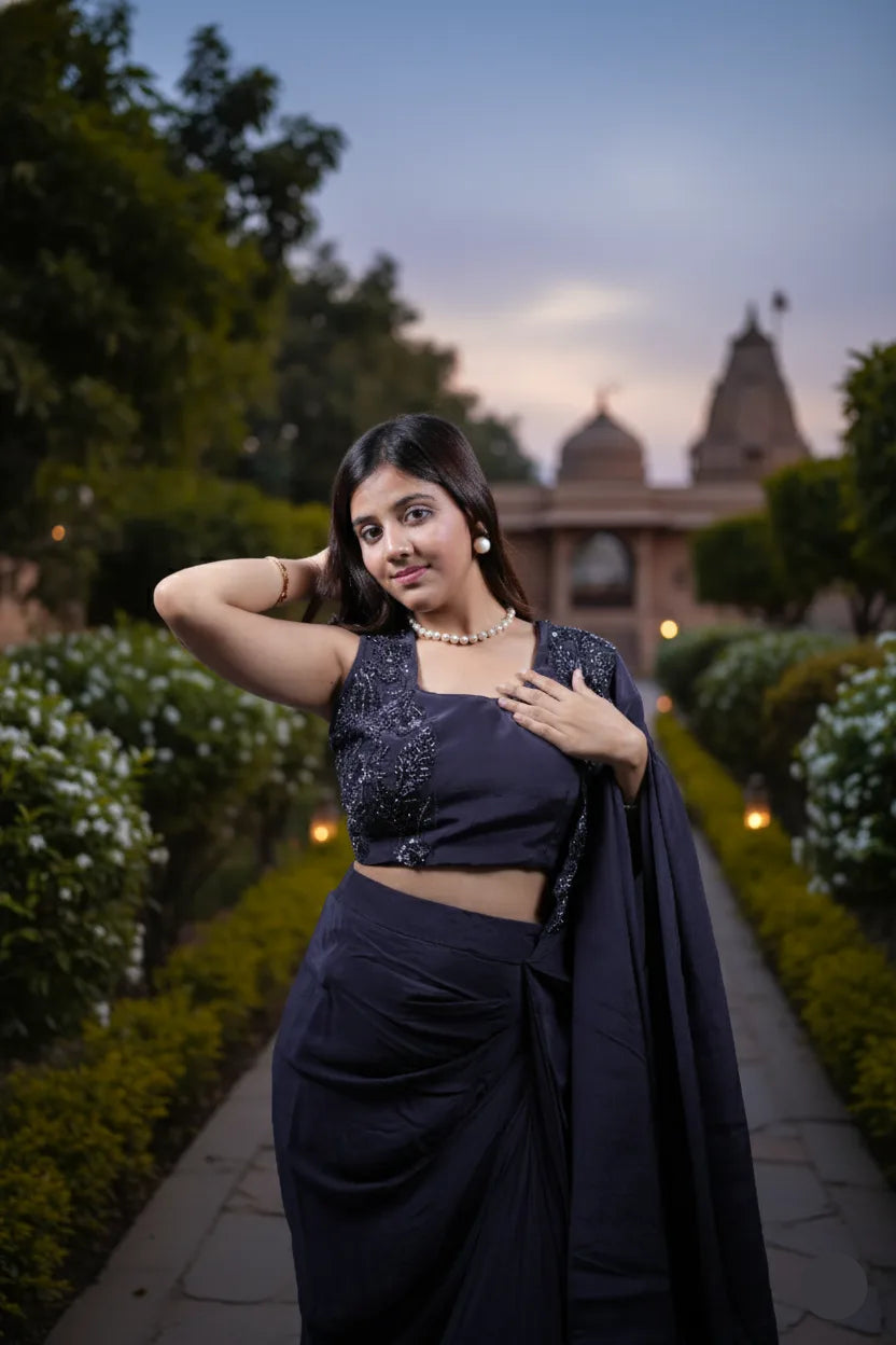 Woman in a dark blue saree standing in a garden with a temple in the background