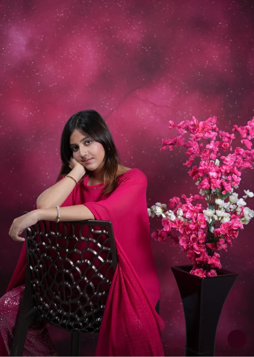 Woman in a pink outfit sitting next to a plant against a pink background