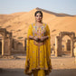 Woman in a yellow traditional outfit standing in a desert with ancient architecture.