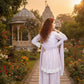 Woman in a white dress standing in a garden with a temple in the background