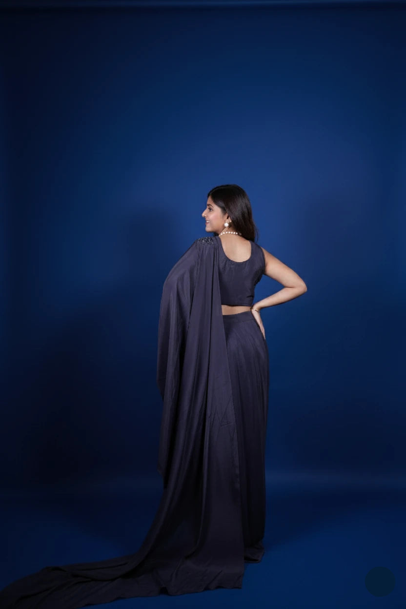 Woman in a dark blue saree with a long train against a solid blue background