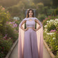 Woman in a lavender outfit with a pink cape standing in a garden.