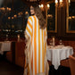 Woman in a long, striped dress walking through a restaurant with a cityscape view.