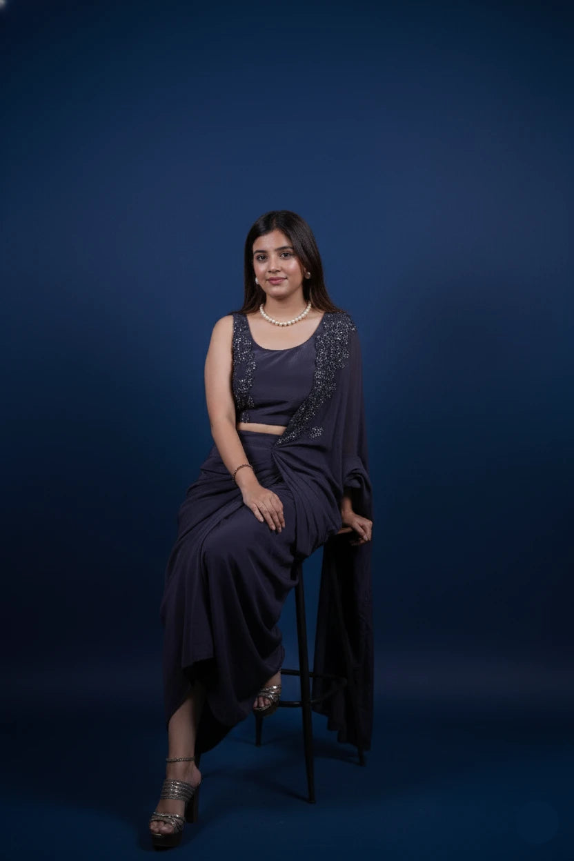 Woman in a dark blue dress sitting on a stool against a blue background