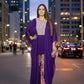 Woman in a purple outfit standing on a city street at night.
