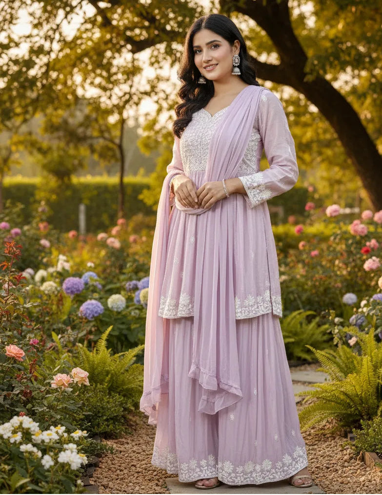 Woman in a light purple traditional outfit standing in a garden with flowers and trees.