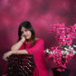 Woman in a pink outfit sitting next to a plant against a pink background