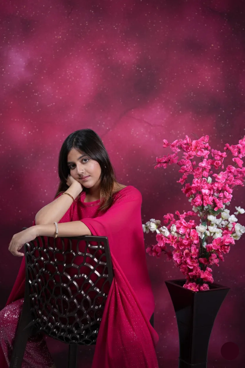 Woman in a pink outfit sitting next to a plant against a pink background