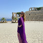 Woman in a purple dress standing in front of ancient ruins with ocean view