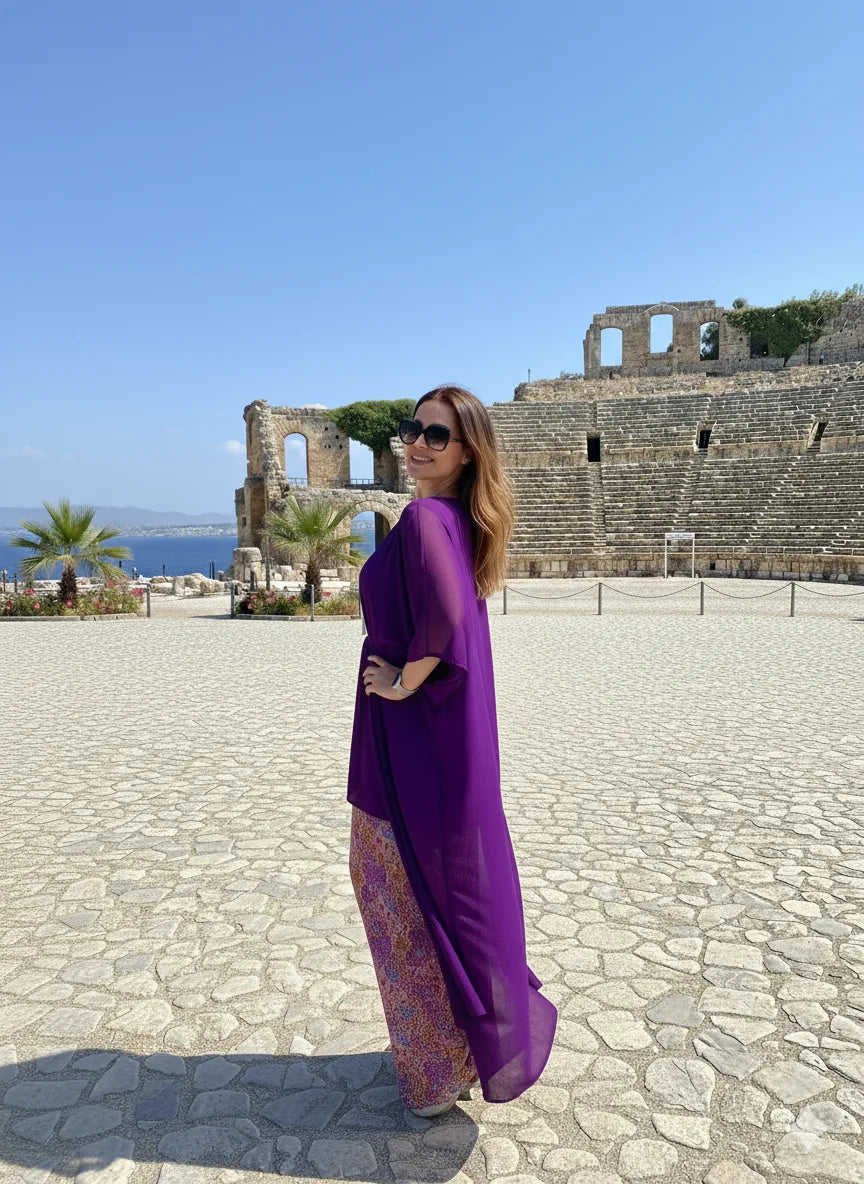 Woman in a purple dress standing in front of ancient ruins with ocean view