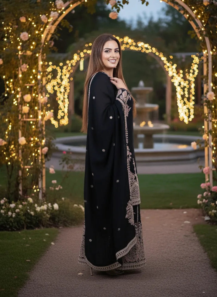 Woman in a black and gold traditional outfit standing in front of a decorative arch with lights and flowers.