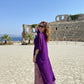 Woman in a purple dress standing in front of ancient ruins with ocean view