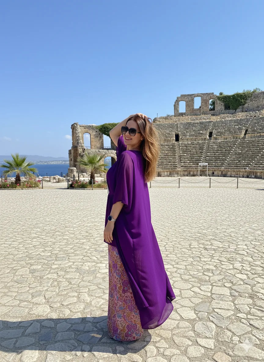 Woman in a purple dress standing in front of ancient ruins with ocean view