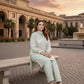 Woman sitting on a bench in an elegant outdoor setting with classical architecture and palm trees.
