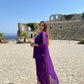 Woman in a purple dress standing in front of ancient ruins with ocean view