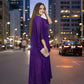 Woman in a purple dress standing on a city street at night.