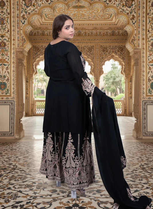 Woman in black traditional outfit with intricate patterns in a ornate indoor setting